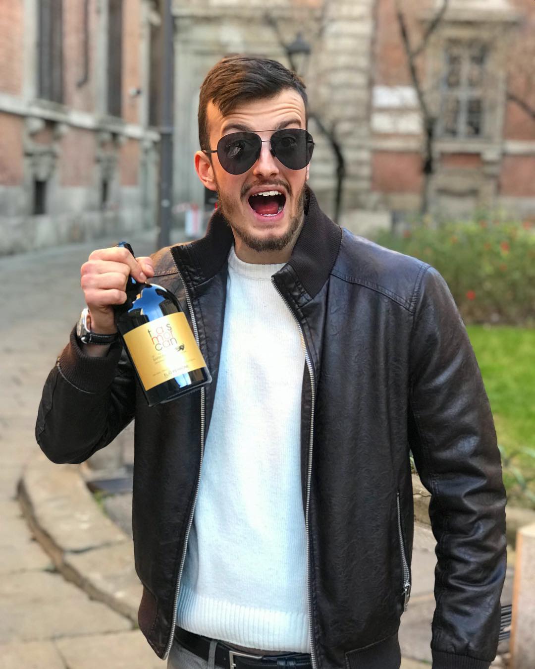 Nicola Pepe smiling outdoors while holding a wine bottle.
